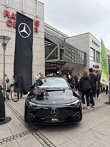 Man sieht einige Teilnehmer und Zuschauer, im Fokus des Bildes steht der CLA Shooting Brake in Schwarz, dahinter eine gro&szlig;e schwarze Fahne mit dem wei&szlig;en Mercedes-Benz Stern.