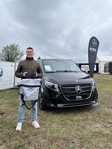 Der Gewinner des zweiten Platzes steht vor einer schwarzen V-Klasse mit einem Mercedes-Benz Rucksack in der Hand.