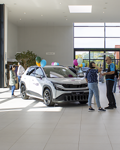 Ein weißer Škoda Epiq mit bunten Luftballons steht im Autohaus. Besucher informieren sich über das neue elektrische SUV.