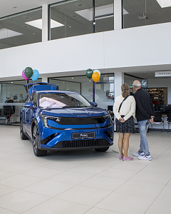 Zwei Besucher betrachten den blauen Škoda Peaq, der mit bunten Luftballons im Showroom der Autowelt Peter ausgestellt ist.