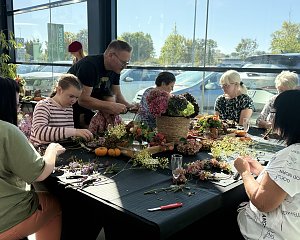 Erwachsene und Kinder sitzen an einer großen Tafel und binden aus Hortensien, Zweigen und weiteren Naturmaterialien herbstliche Kränze.