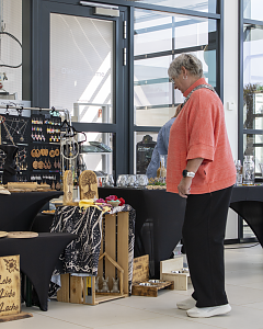 Besucherin betrachtet einen Marktstand mit handgefertigtem Schmuck, Holzdekorationen und weiteren Kunsthandwerksartikeln.