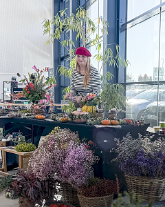 Floristin hinter einem herbstlich dekorierten Stand mit Blumensträußen, Gestecken, Kürbissen und Trockenblumen.