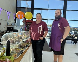 Zwei Personen vom HAPPINO Freizeit- und Erlebnis-Center stehen hinter einem Verkaufsstand mit Kuchen und Süßigkeiten.