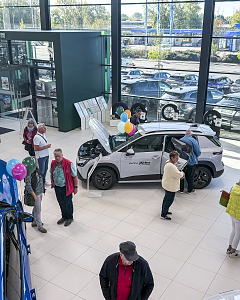 Besucher informieren sich im Škoda-Autohaus über ein weißes Fahrzeug mit geöffneter Motorhaube und weiteren ausgestellten Modellen im Hintergrund.
