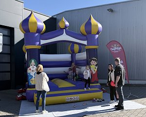 Kinder spielen bei sonnigem Wetter auf einer großen lila-gelben Hüpfburg auf dem Außengelände der Autowelt Peter.