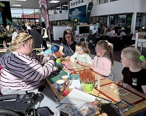 Kinder und Erwachsene gestalten gemeinsam kreative Bastelarbeiten an einem großen Tisch während des Familienprogramms im Škoda-Autohaus.