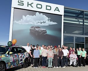 Gruppenfoto des Teams und der Beteiligten vor dem Škoda-Autohaus mit farbenfroh foliertem Aktionsfahrzeug und großer Škoda-Werbefläche.