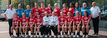 Gruppenfoto des Thüringer Handball Clubs (THC) vor dem Autohaus Peter in Erfurt. In zwei Reihen posieren rund 20 Spielerinnen in roten Trikots gemeinsam mit Trainerteam und Partnern. Links und rechts außen stehen Helmut Peter und Robert Böhm. Im Hintergrund mehrere Fahrzeuge mit „Autohaus Peter“-Branding. Das THC-Team lächelt geschlossen in die Kamera. (Autohaus Peter)