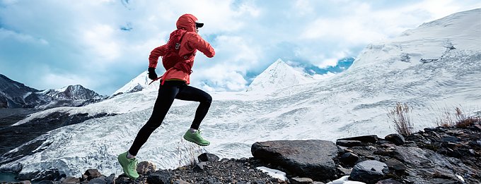 Frau mit roter Jacke rennt einen schneebedeckten Berg hinauf