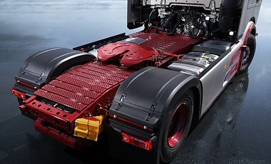Heckbereich der Lkw-Zugmaschine von schr&auml;g oben. Rote Sattelkupplung und rot lackierter Rahmen. Gro&szlig;e, schwarze Kotfl&uuml;gel &uuml;ber den Hinterreifen. Seitliche Aluminium-Tanks. Der Lkw steht auf einer nassen, dunkel spiegelnden Stra&szlig;e.